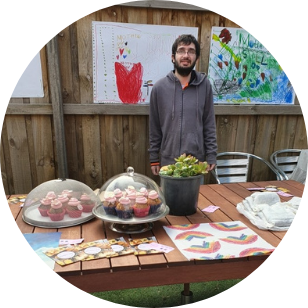 Ane standing in front of the mothers day stall, with posters on the fence behind him.