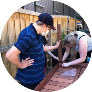 Mikey dressed in a blue shirt and Molly with her hair in a ponytail working on an upside down table. Mikey is holding the legs and Molly is tightening the screws