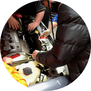 Participants working on the engine of a car, while being watched by the instructor